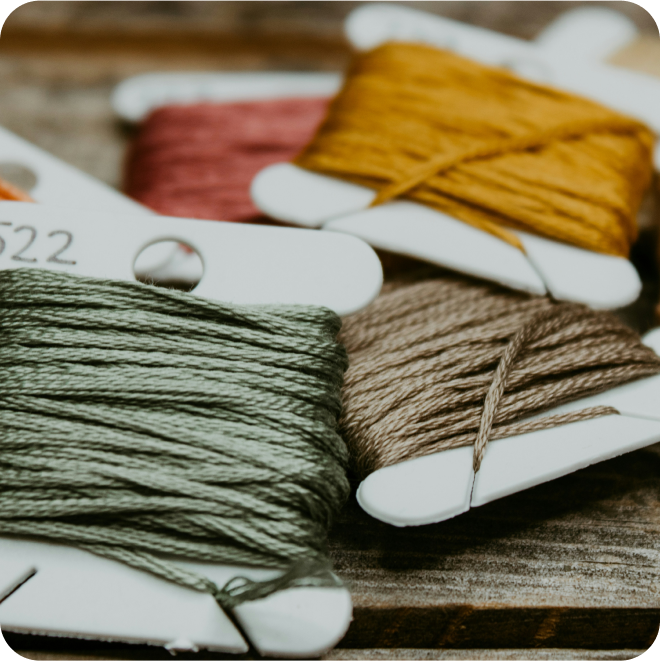 Multiple colored thread spools, including green, tan, mustard, and red, laid on a wooden surface.